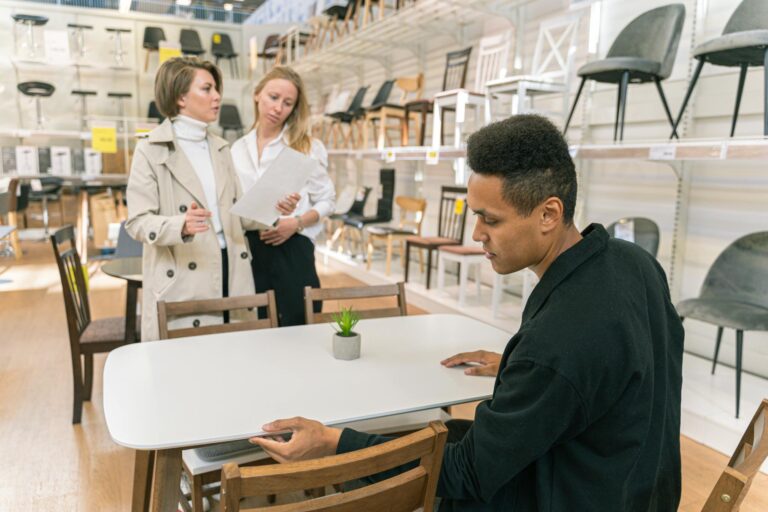 A professional discussion takes place in a well-lit furniture store showroom with diverse employees.